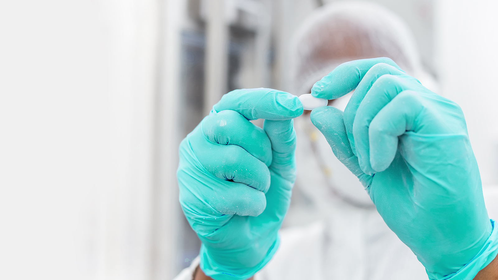 Drug manufacturer wearing PPE and holding a white pill with their thumbs and index fingers