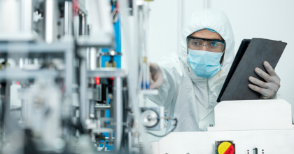 Male in laboratory is looking at equipment and holding a black folder.