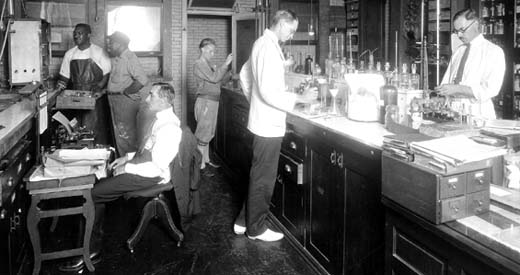 Several men and one woman working at a lab bench and monitoring laboratory equipment