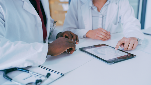 Photo of two doctors sitting at desk looking at iPad.