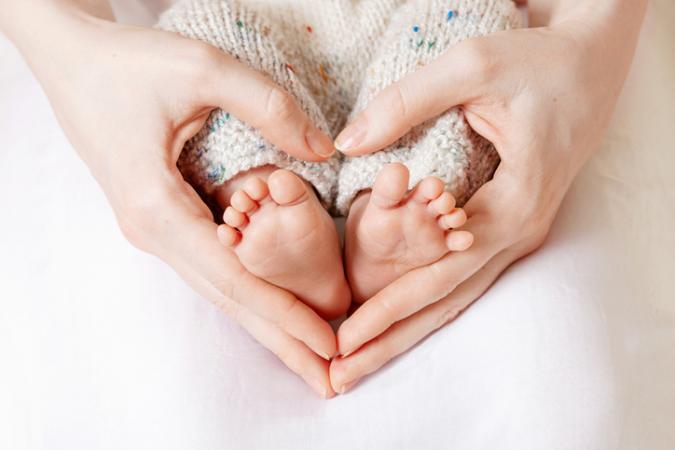 Tiny Newborn Baby's feet on female Heart Shaped hands closeup