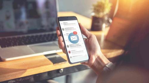 Hand holding smartphone with new email notification, with computer in background