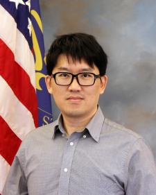 Man with glasses posing in front of American flag