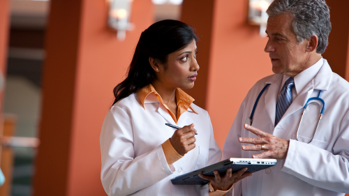 Two doctors talking, one holding a tablet and pen