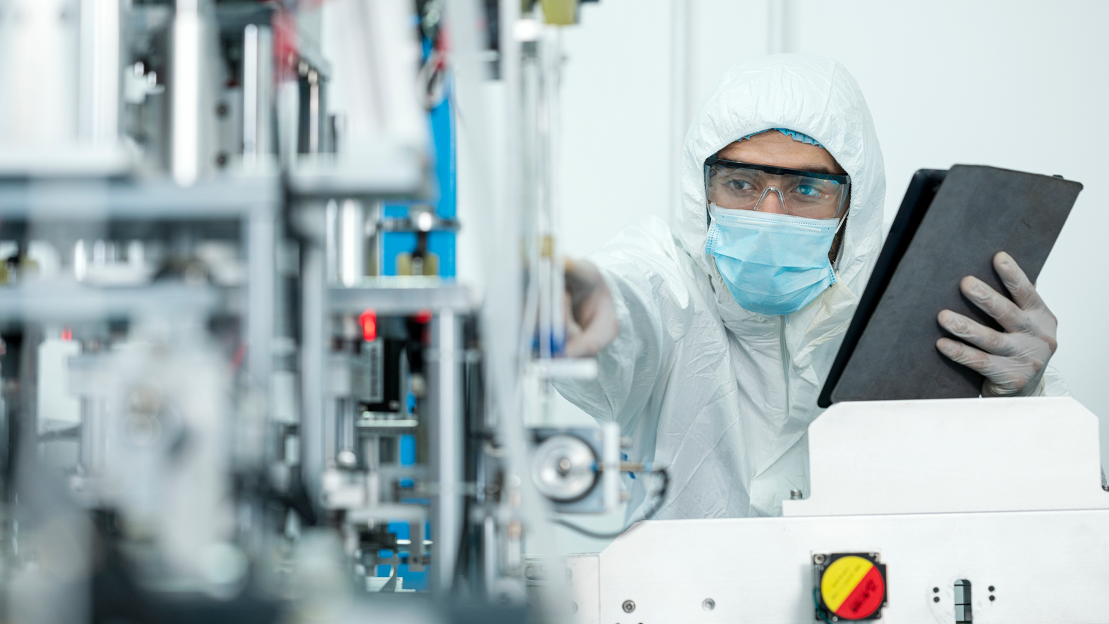 Male in laboratory is looking at equipment and holding a black folder.