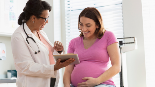 Photo of female health care specialist talking with pregnant woman in exam room.