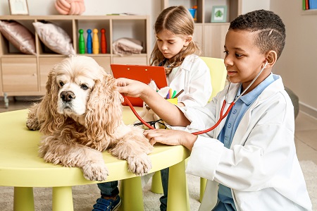 Dos niños se disfrazan de veterinarios en sala de juegos. Un perro tierno está acostado en una mesa. Los niños pretenden observar los signos vitales del perro..