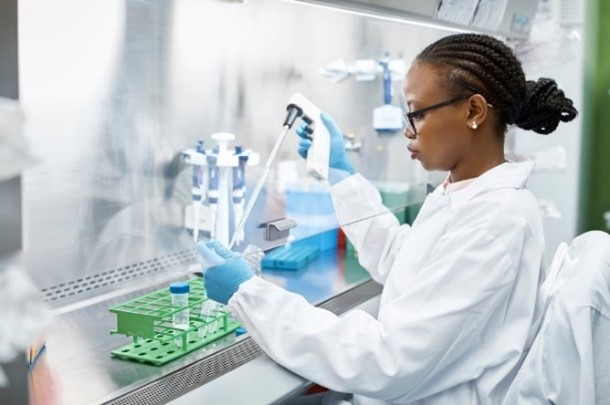 A woman working in a laboratory and putting a liquid substance into a vile.