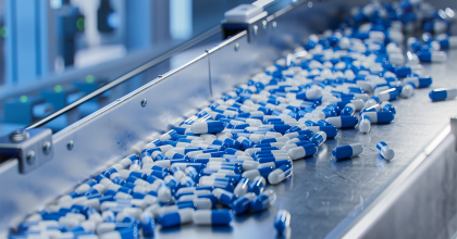 Blue capsules on conveyor at modern pharmaceutical factory.