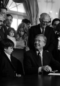 black and white photo of president sitting at desk surrounded by people