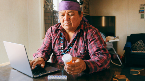 A mature Indigenous Navajo man, refilling a medicine prescription online from home with a laptop computer.