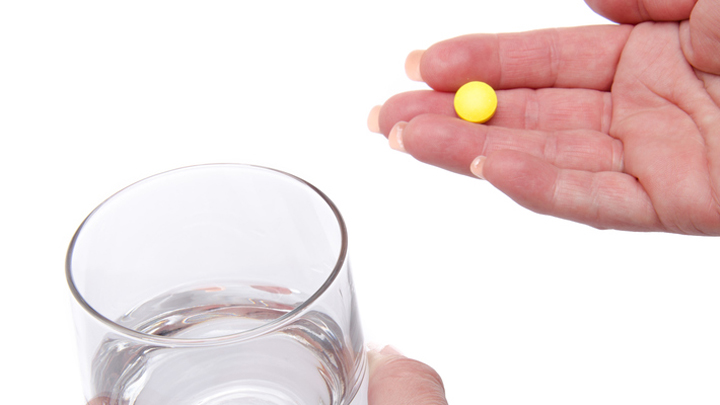 Hands holding a pill and a glass of water